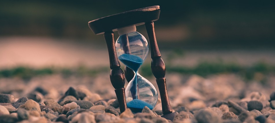 Hour glass with blue sand standing in pebbles