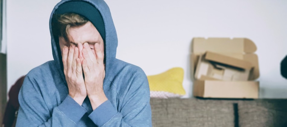 Man in blue hoody covering face with both hands | Side Effects of Modvigil